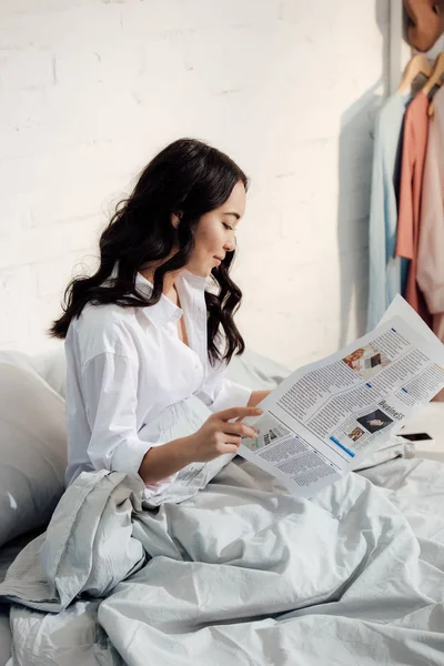 朝のベッドに座って新聞を読んで美しい若いアジア女性 — ストック写真