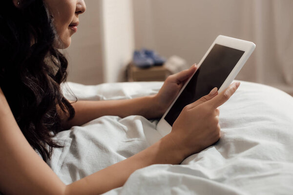 cropped shot of attractive girl lying on bed and using digital tablet with blank screen