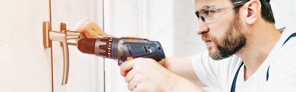 panoramic view of focused male handyman in goggle repairing window handle with electric drill 