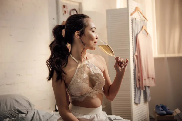 ワインを飲むと ベッドルームに目をそむけるランジェリーで美しい幸せな若いアジア女性 — ストック写真