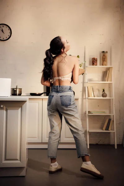 年轻女子在胸罩和牛仔裤子举行花束在家里的背景下的看法 — 图库照片
