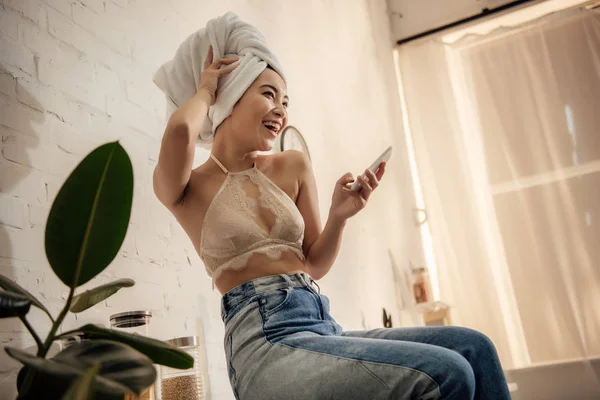 キッチンでスマート フォンを使用して頭の上のタオルで美しい幸せな女の子のローアングル ビュー — ストック写真