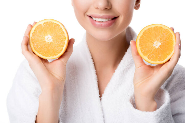 partial view of smiling woman in white bathrobe holding oranges isolated on white