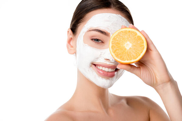 attractive woman with facial skin care mask holding orange in front of face isolated on white