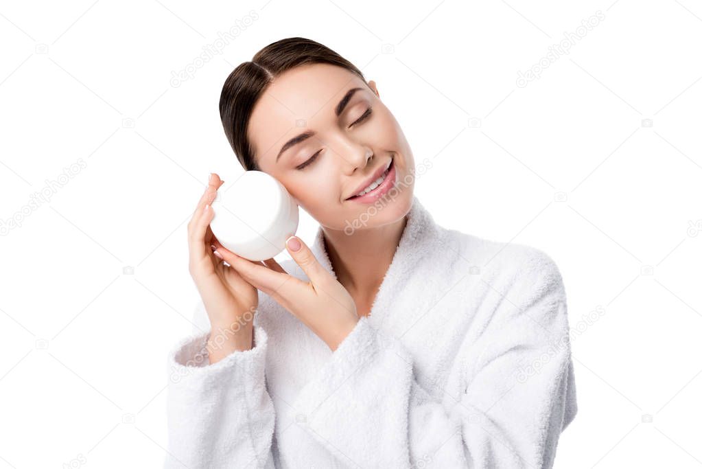 woman in bathrobe with eyes closed holding face cream isolated on white