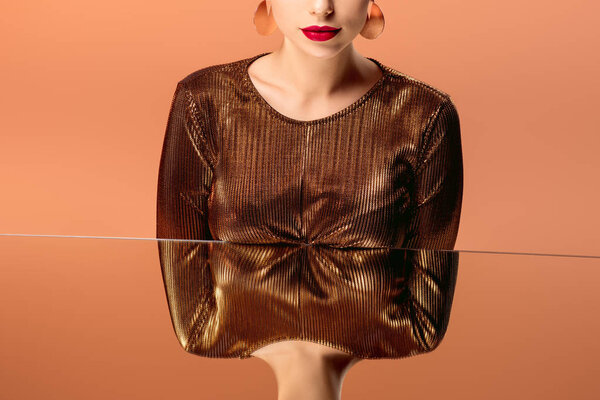 обрезанный вид женщины в золотой одежде с красными губами и зеркальным отражением, изолированным на оранжевом
