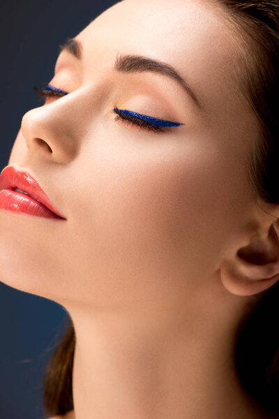 selective focus of beautiful woman with glamorous makeup and eyes closed isolated on blue
