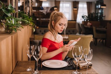 restoranda oturan ve smartphone vasıl seyir kırmızı elbiseli çekici kadın