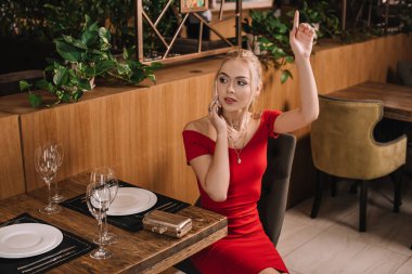 restoranda oturan ve el yükselterek kırmızı elbiseli çekici kadın