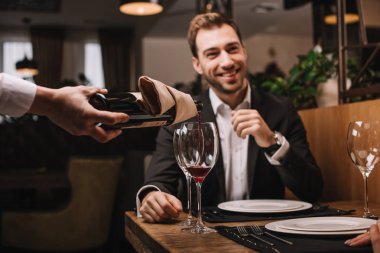 gülümseyen ve restoranda oturan takım elbiseli çekici adamın seçici odak