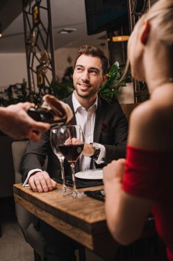 selective focus of handsome man looking at waiter pouring red wine into glass  clipart