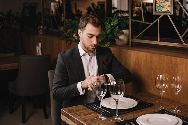 handsome man in suit waiting for girlfriend in restaurant and looking at watch