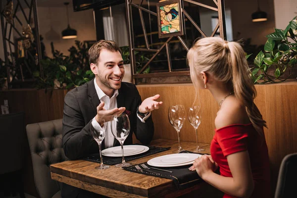 Schöner Freund Lächelt Und Gestikuliert Neben Freundin Rotem Kleid — Stockfoto