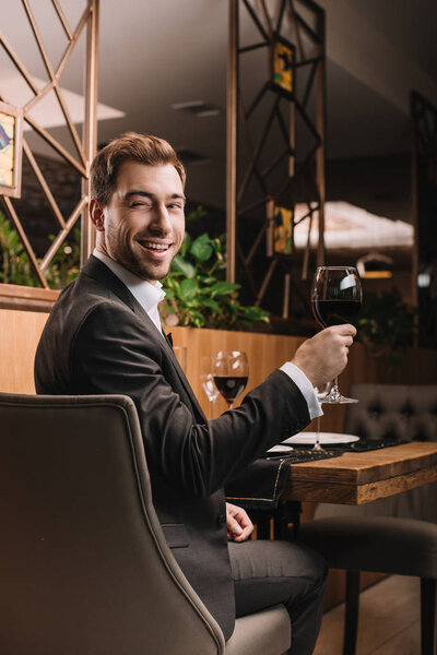 handsome man holding glass with red wine while sitting in restaurant 