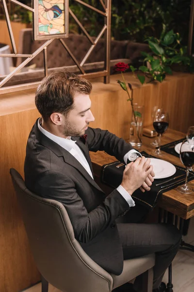 Hombre Guapo Mirando Reloj Mientras Está Sentado Restaurante —  Fotos de Stock