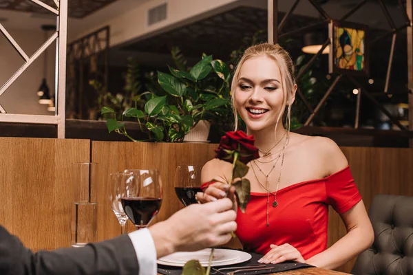 レストランに座っている彼氏の手で赤いバラを見ている陽気なガール フレンドの選択と集中 — ストック写真