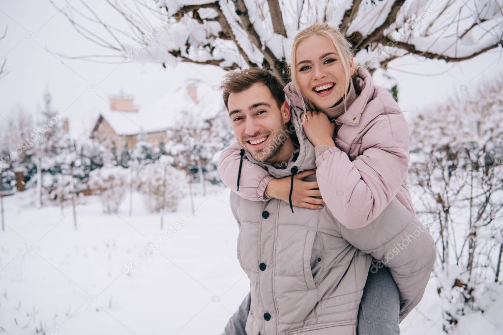 smiling man carrying attractive blonde woman on back in winter 
