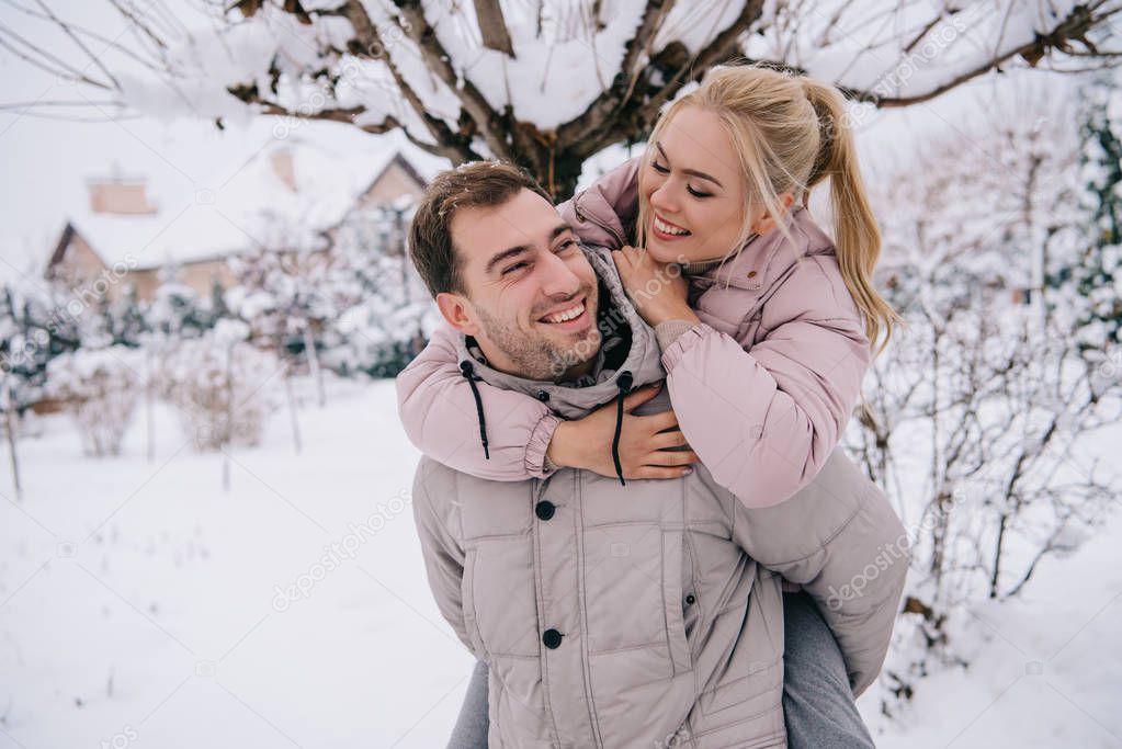 cheerful boyfriend carrying attractive blonde girl on back in winter  