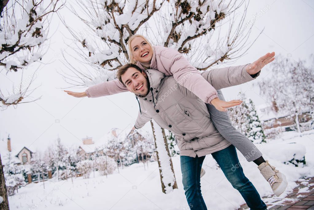 playful boyfriend carrying attractive girl on back in winter  