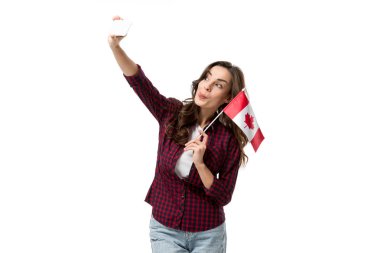 woman holding canadian flag, sticking tongue out and taking selfie on smartphone isolated on white clipart
