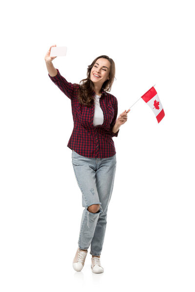 happy woman holding canadian flag and taking selfie on smartphone isolated on white