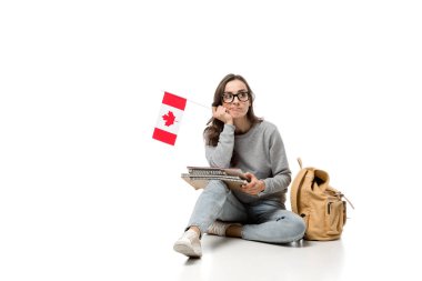 pensive female student sitting with canadian flag and notebooks isolated on white clipart