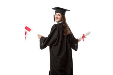 attractive smiling female student in academic gown holding canadian flag and diploma isolated on white