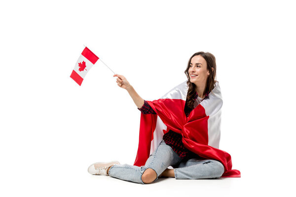 smiling woman covered in canadian flag holding maple leaf flag isolated on white