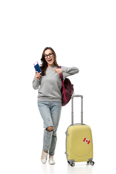 female student with suitcase pointing with finger at passport and air tickets isolated on white, studying abroad concept