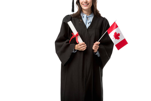 partial view of female student in academic gown holding canadian flag and diploma isolated on white