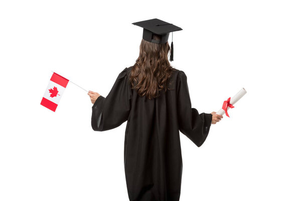 back view of female student in academic gown and mortarboard holding canadian flag with diploma isolated on white
