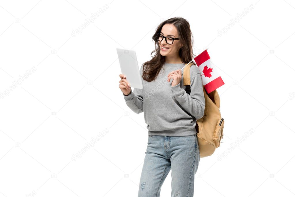 smiling female student in glasses holding canadian flag and using digital tablet isolated on white