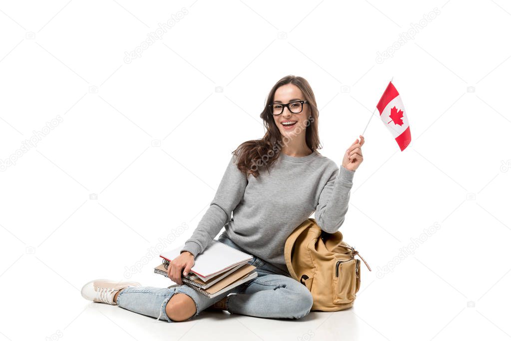 happy female student sitting with canadian flag and notebooks isolated on white