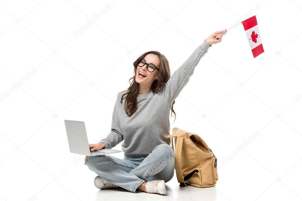 female student sitting with laptop and cheering with canadian flag isolated on white