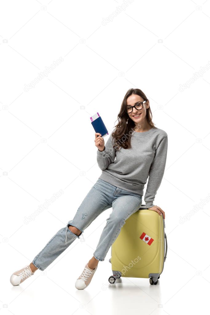 happy woman sitting on suitcase with passport and air tickets isolated on white, travel concept