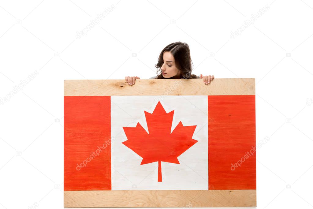 woman sitting behind wooden board with canadian flag and looking away isolated on white
