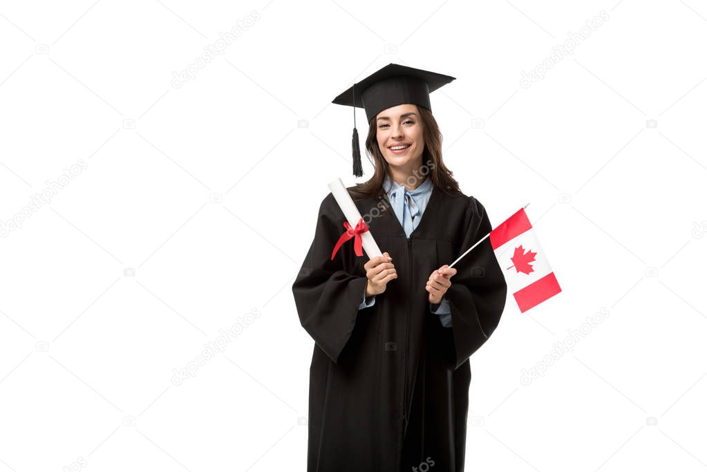 female student in academic gown looking at camera and holding canadian flag with diploma isolated on white