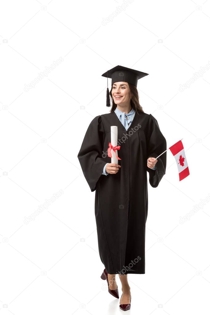 cheerful female student in academic gown holding canadian flag and diploma isolated on white