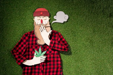 cardboard man in plaid shirt holding cannabis and smoking on green grass background, marijuana legalization concept clipart