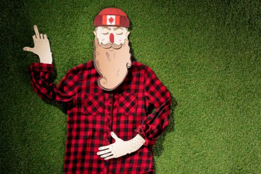 cardboard man in plaid shirt and hat with maple leaf showing middle finger on green grass background clipart
