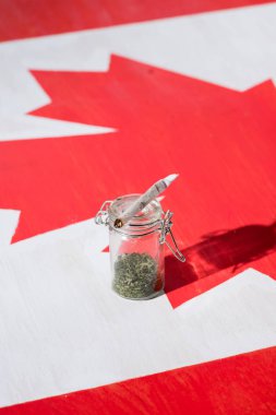 selective focus of cannabis in glass jar with joint on canadian flag, marijuana legalization concept clipart