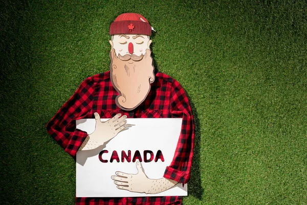 格子縞のシャツと緑の草の背景に カナダ 単語とホワイト ボードを保持している帽子のダン ボール男 — ストック写真