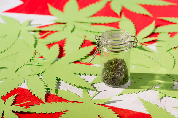 paper marijuana leaves on canadian flag with cannabis in glass jar, marijuana legalization concept