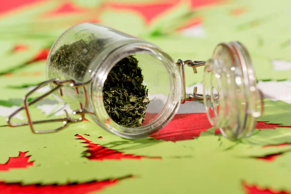 cannabis in glass jar with paper leaves on background, marijuana legalization concept