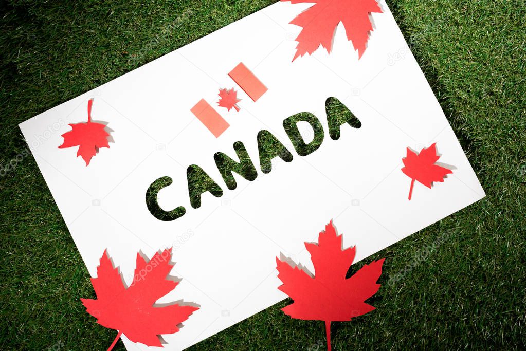 white board with cut out word 'canada' on green grass background  with maple leaves and canadian flag