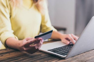 cropped view of woman holding credit card near laptop at home