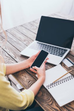 smartphone ile boş ekran laptop yakınındaki tutan kadın görünümünü kırpılmış
