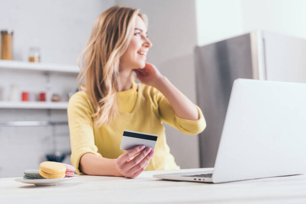 selective focus of credit card in hand of blonde woman near laptop 