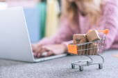 selective focus of small cart with toy paper boxes with woman using laptop on background