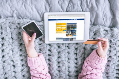 kredi kartı ve rezervasyon uygulaması ile dijital tablet yakınındaki smartphone ekranında tutan kadın görünümünü kırpılmış